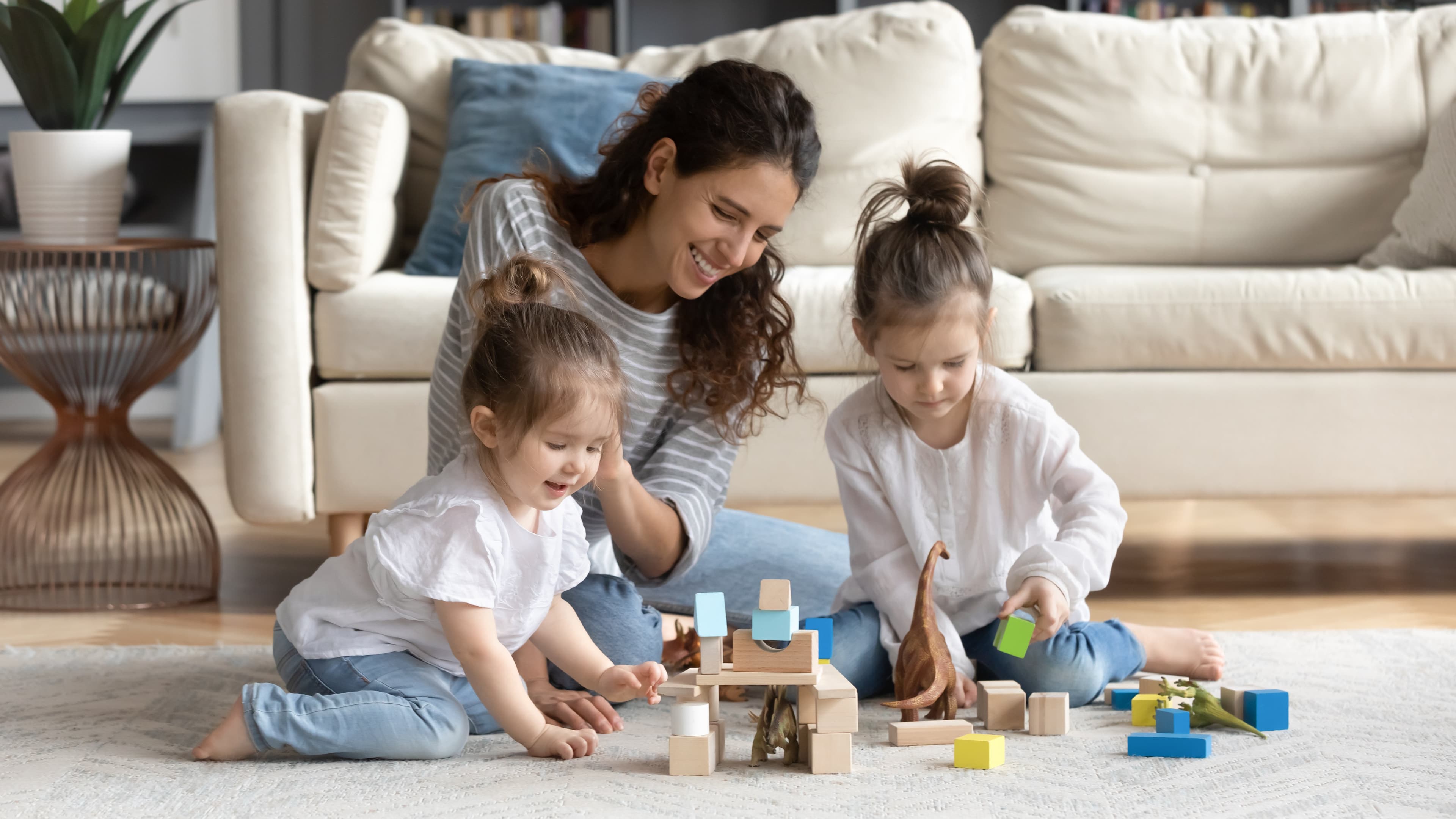 An image of a mother playing with her two daughters on the floor of their living room 